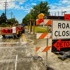 Construction site with sign in the foreground that reads 'Road Closed Detour'